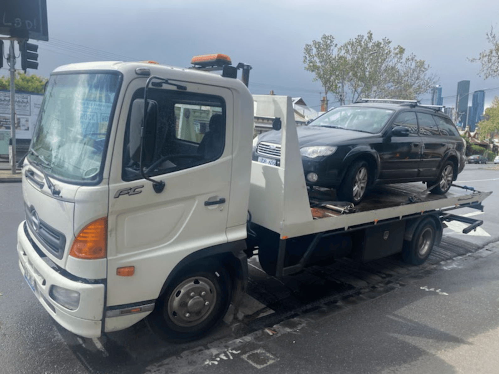 A Subaru is being towed in the CBD of Melbourne.