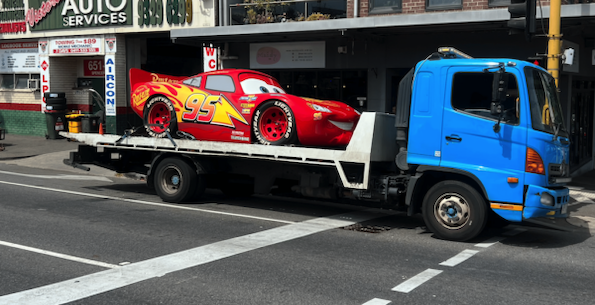 A tow truck towing a novelty car for a kid's party.